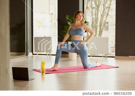 Portrait of young pregnant woman doing yoga on mat indoors on a daytime. Online training lessons on laptop Portrait of young pregnant woman doing yoga on mat indoors on a daytime. Online training lessons on laptop 96038200