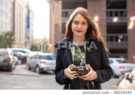 Outdoor autumn smiling lifestyle portrait of pretty young woman, having fun in the city with camera, travel photo of photographer. Outdoor autumn smiling lifestyle portrait of pretty young woman, having fun in the city with camera, travel photo of photographer. 96038440