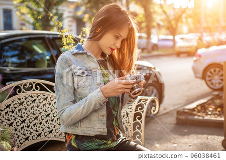 Outdoor autumn smiling lifestyle portrait of pretty young woman, having fun in the city with camera, travel photo of photographer. Outdoor autumn smiling lifestyle portrait of pretty young woman, having fun in the city with camera, travel photo of photographer. 96038461