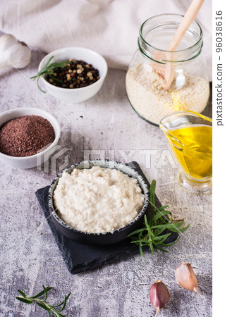 Sesame tahini with black salt in a bowl and cooking ingredients on the table. Vertical view 96038616