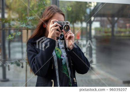 Outdoor autumn smiling lifestyle portrait of pretty young woman, having fun in the city with camera, travel photo of photographer. 96039207