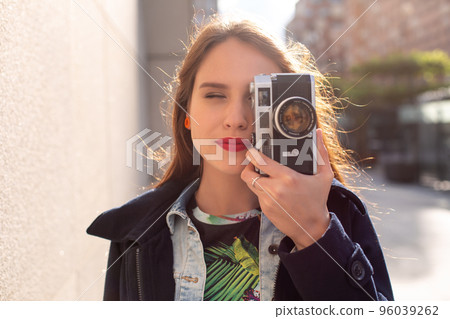 Outdoor autumn smiling lifestyle portrait of pretty young woman, having fun in the city with camera, travel photo of photographer. Outdoor autumn smiling lifestyle portrait of pretty young woman, having fun in the city with camera, travel photo of photographer. 96039262