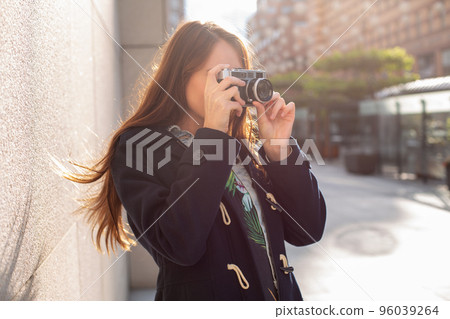 Outdoor autumn smiling lifestyle portrait of pretty young woman, having fun in the city with camera, travel photo of photographer. Outdoor autumn smiling lifestyle portrait of pretty young woman, having fun in the city with camera, travel photo of photographer. 96039264