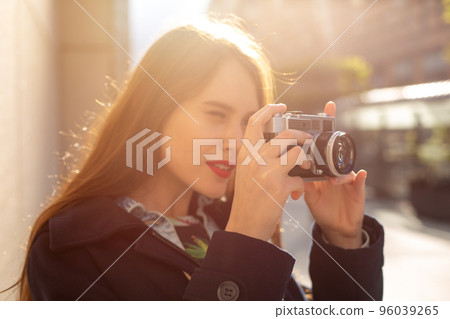 Outdoor autumn smiling lifestyle portrait of pretty young woman, having fun in the city with camera, travel photo of photographer. Outdoor autumn smiling lifestyle portrait of pretty young woman, having fun in the city with camera, travel photo of photographer. 96039265