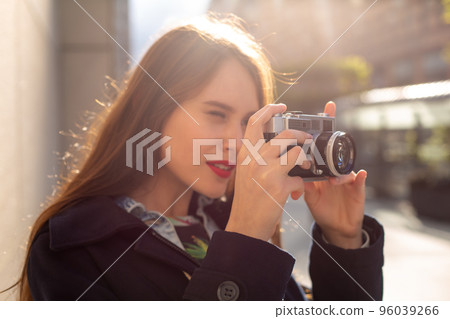 Outdoor autumn smiling lifestyle portrait of pretty young woman, having fun in the city with camera, travel photo of photographer. 96039266