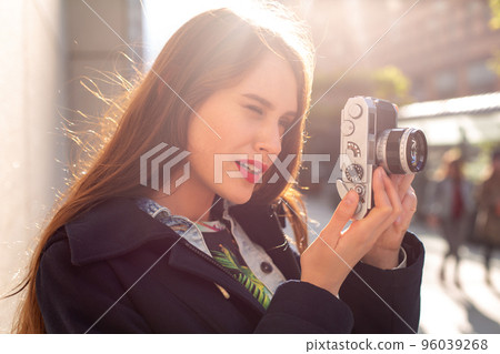 Outdoor autumn smiling lifestyle portrait of pretty young woman, having fun in the city with camera, travel photo of photographer. Outdoor autumn smiling lifestyle portrait of pretty young woman, having fun in the city with camera, travel photo of photographer. 96039268