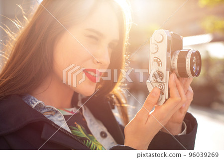 Outdoor autumn smiling lifestyle portrait of pretty young woman, having fun in the city with camera, travel photo of photographer. Outdoor autumn smiling lifestyle portrait of pretty young woman, having fun in the city with camera, travel photo of photographer. 96039269