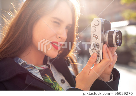 Happy hipster girl making photo with retro camera on city street. Sun flare Happy hipster girl making photo with retro camera on city street. Sun flare 96039270