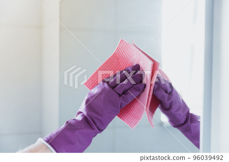Cropped view of housekeeper woman hand in purple rubber gloves polishing mirror with pink cloth rag cleaner while cleaning bathroom at home. Housekeeping and cleaning service. Clean house, cleanliness Cropped view of housekeeper woman hand in purple rubber gloves polishing mirror with pink cloth rag cleaner while cleaning bathroom at home. Housekeeping and cleaning service. Clean house, cleanliness 96039492