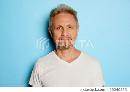 Portrait of mature man in white T-shirt posing, looking at camera isolated over blue studio background 96040253