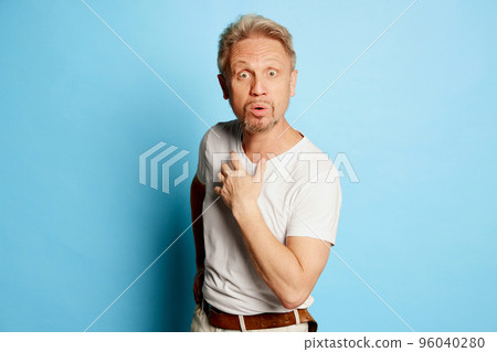 Portrait of mature man in white T-shirt posing isolated over blue studio background. Shocked face 96040280