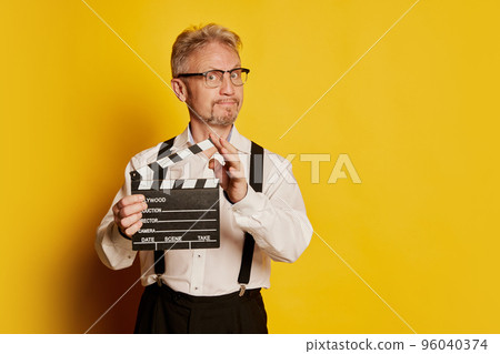 Portrait of mature man in stylish classical clothes posing isolated over yellow studio background. Movie scenario 96040374