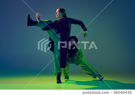 Two dancers, stylish fashionable dance couple dancing contemporary dance on colorful gradient blue-green background in neon light. Concept of art, creativity, movement, style and fashion, action. Two dancers, stylish fashionable dance couple dancing contemporary dance on colorful gradient blue-green background in neon light. Concept of art, creativity, movement, style and fashion, action. 96040436