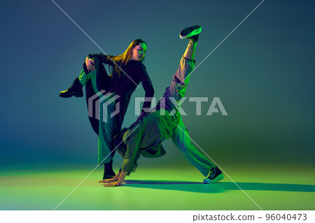 Two dancers, stylish fashionable dance couple dancing contemporary dance on colorful gradient blue-green background in neon light. Concept of art, creativity, movement, style and fashion, action. 96040473