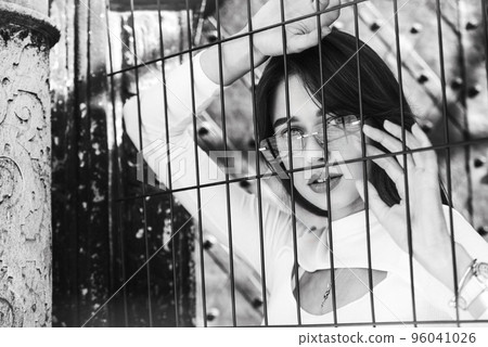 Close-up portrait of woman a in a white blause near a metal grid Close-up portrait of woman a in a white blause near a metal grid 96041026
