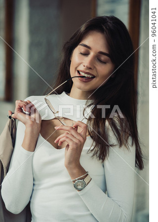 beautiful brunette girl in a sunglasses dressed in white blouse with a beige coat in hands. Stylish trendy fashion outlook beautiful brunette girl in a sunglasses dressed in white blouse with a beige coat in hands. Stylish trendy fashion outlook 96041041