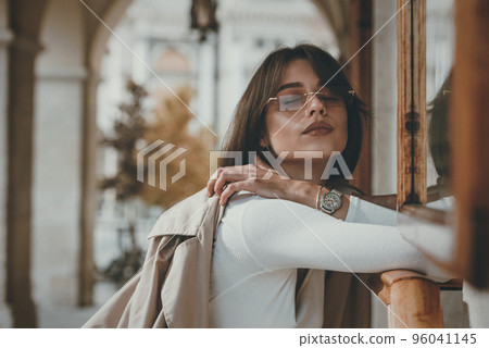 beautiful brunette girl in a sunglasses dressed in white blouse with a beige coat in hands. Stylish trendy fashion outlook 96041145