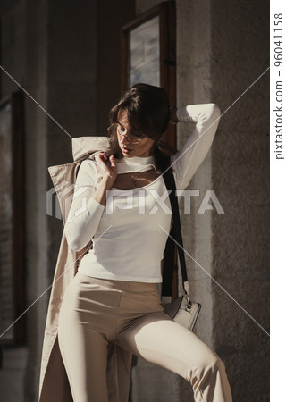 beautiful brunette girl in a sunglasses dressed in white blouse with a beige coat in hands. Stylish trendy fashion outlook 96041158