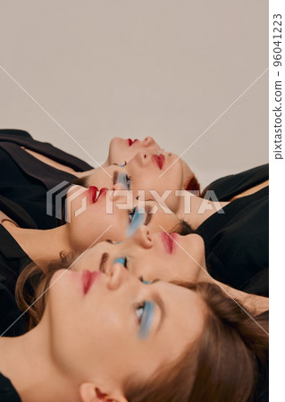 Portrait of young beautiful women in black jackets lying on floor closely, posing over grey background 96041223