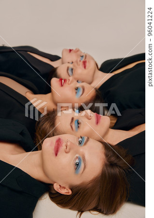 Portrait of young beautiful women in black jackets with bright makeup posing, lying on floor over grey background 96041224
