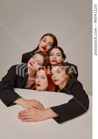 Portrait of young beautiful women in black jackets with red lipstick, blue eyeshadow makeup posing over grey background Portrait of young beautiful women in black jackets with red lipstick, blue eyeshadow makeup posing over grey background 96041229