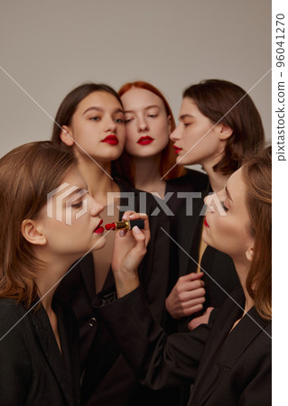 Portrait of young beautiful women in black jackets and red lipstick, applying makeup, posing over grey background 96041270