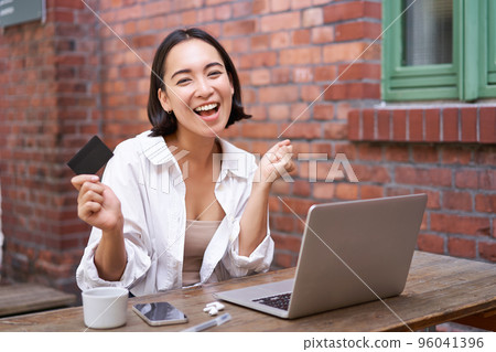 Enthusiastic asian girl sitting with credit card and laptop, paying contactless, shopping online via computer 96041396