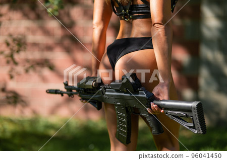 Close-up of a female buttocks in a bikini with a machine gun outdoors. 96041450
