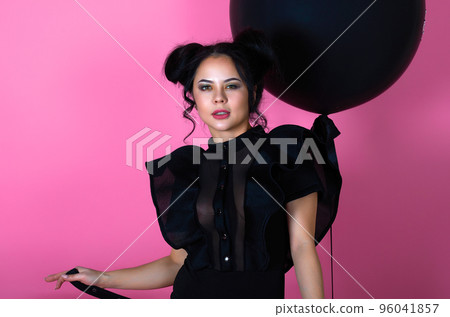 beauty portrait of a brunette girl in a black dress on a pink background with a black inflatable ball 96041857