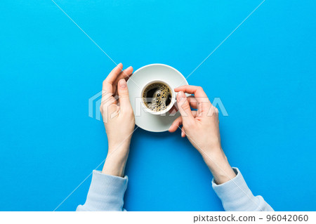 Minimalistic style woman hand holding a cup of coffee on Colored background. Flat lay, top view cappuccino cup. Empty place for text, copy space. Coffee addiction. Top view, flat lay 96042060