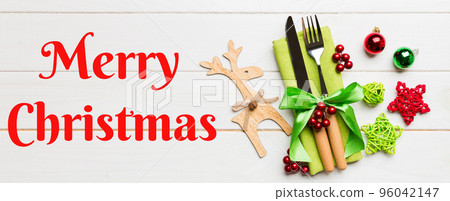 Merry Christmas text. New year set Banner of fork and knife on napkin. Top view of christmas decorations and reindeer on wooden background. Holiday family dinner concept 96042147