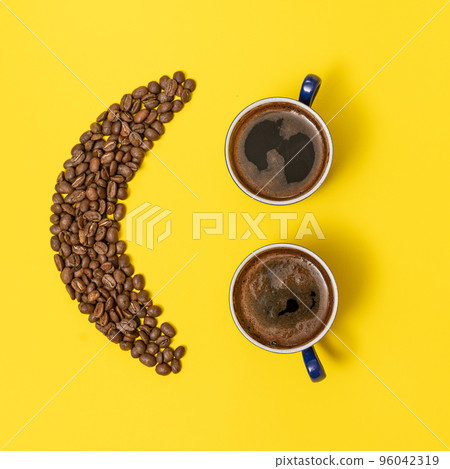 two cups of coffee and an emoticon made of coffee beans on a yellow background. two cups of coffee and an emoticon made of coffee beans on a yellow background. 96042319