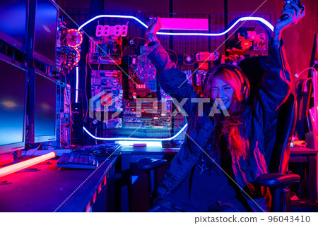Winning. Happy Gamer young plays online video games computer she raises hands to wins tournament, young woman in gaming headphones playing video game online at home feel excited, E-Sport concept 96043410