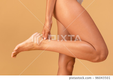 High heel syndrome. Closeup of caucasian young woman massaging her injured ankle, posing over beige background High heel syndrome. Closeup of caucasian young woman massaging her injured ankle, posing over beige background 96043501