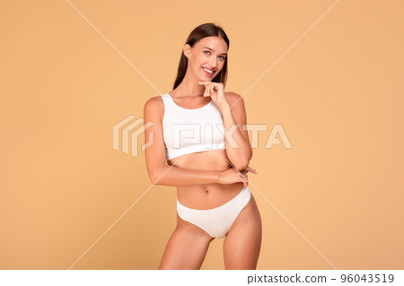 Body slimming concept. Happy caucasian woman with fit figure in white underwear smiling at camera, beige background 96043519