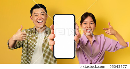 Smiling Asian Man And Woman Demonstrating Empty Smartphone With Big White Screen Smiling Asian Man And Woman Demonstrating Empty Smartphone With Big White Screen 96043577