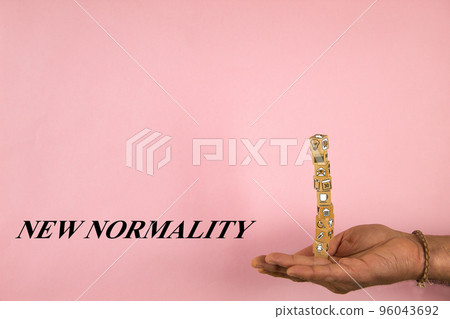 hand holding a stack of shaped wooden blocks with text of new normality on a pink background 96043692