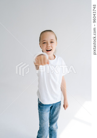 Vertical portrait of brave smiling little girl with broken hand wrapped in white plaster bandage playing gesturing with injured wrist on light isolated background. Concept of child healthcare. 96043748