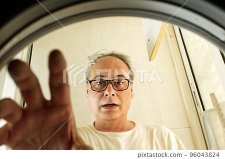 mature man taking clothes out of the washing machine seen from inside mature man taking clothes out of the washing machine seen from inside 96043824