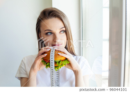 Woman with burger and measuring tape while dieting 96044101
