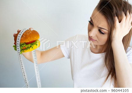 Woman with burger and measuring tape while dieting 96044105