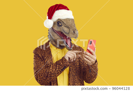 Funny man wearing dinosaur mask, Christmas hat and leopard suit using mobile phone 96044128