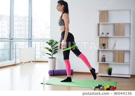 Sporty young woman doing squat morning exercise alone in living room 96044136