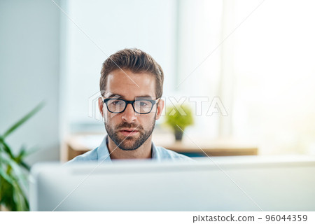 Busy at work as usual. Shot of a young businessman working on a computer in an office. 96044359