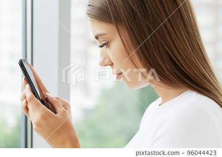 Head shot close up young shocked woman looking at mobile phone screen Head shot close up young shocked woman looking at mobile phone screen 96044423