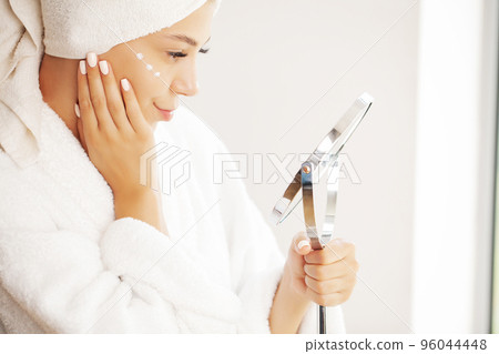Studio shot of beautiful young woman applying moisturizer cream onto her face Studio shot of beautiful young woman applying moisturizer cream onto her face 96044448