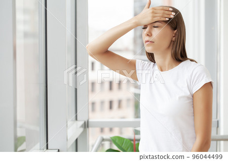 Beautiful stressed young office worker sitting at desk holding head because of pain in office 96044499