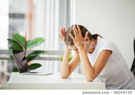 Beautiful stressed young office worker sitting at desk holding head because of pain in office Beautiful stressed young office worker sitting at desk holding head because of pain in office 96044539