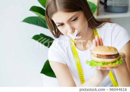 Woman with a taped mouth sits at a table with fast food. 96044616