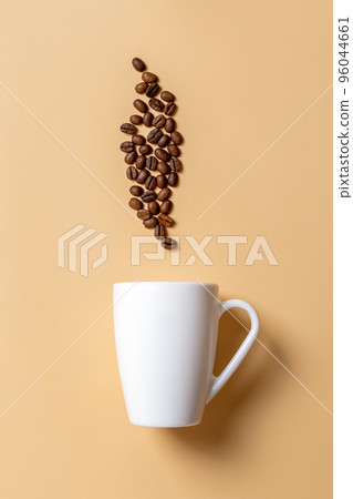 White mug and roasted coffee beans above it over beige background. 96044661